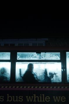 people are standing on the side of a bus in front of some windows at night