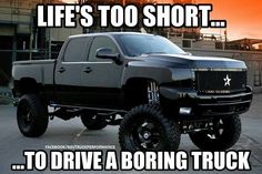 a large black truck parked in front of a factory with an orange sky behind it