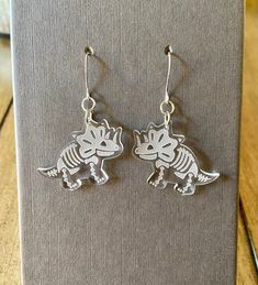 the dinosaur earrings are on display in front of a gray book with silver earwires