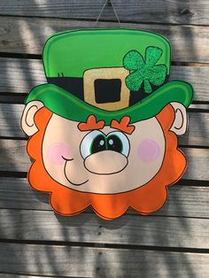 a st patrick's day sign with a green hat and clover on it hanging from the side of a wooden fence