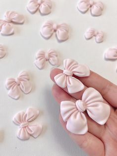 a hand is holding several pink bows on white paper with small ones in the background