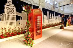 a red phone booth decorated with flowers and greenery at an indoor christmas event in the city