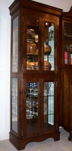 a wooden china cabinet with glass doors on the front and bottom, in a room with carpeted flooring