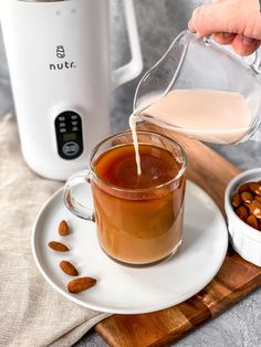 a person pours coffee into a glass mug on a plate with almonds next to it