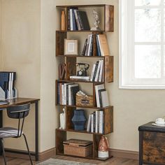 a wooden book shelf filled with books next to a desk and chair in front of a window