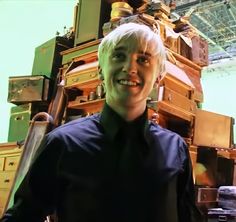 a man with blonde hair standing in front of stacks of trunks and boxes smiling at the camera