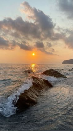 the sun is setting over the ocean with rocks in the foreground and waves crashing on the shore