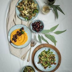 a table topped with plates of food and bowls of salad next to glasses of wine