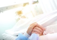 a close up of a person laying in a hospital bed holding the hand of another person