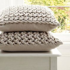 two knitted pillows stacked on top of each other in front of a windowsill