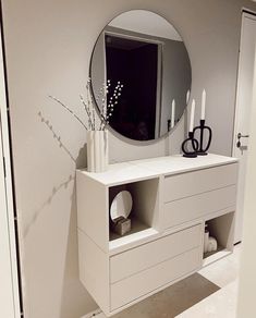 a white dresser with candles and vases on it next to a wall mounted mirror