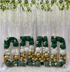 the letters are made out of balloons and green, white and gold balls in front of a backdrop