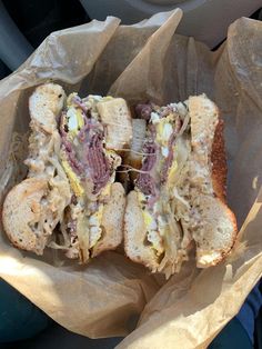 a sandwich with meat, cheese and mustard on it in a wrapper next to a car steering wheel