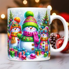 a coffee mug with two snowmen and presents on the table next to christmas decorations