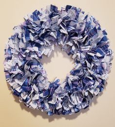 a blue and white wreath made out of newspaper strips hanging on a wall in front of a beige wall