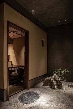 an empty room with rocks and plants in the corner, next to a door that leads into a dining area