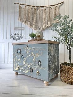 a blue chest with buttons on it in front of a potted plant and wall hangings