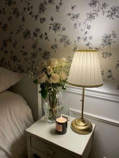 a vase with flowers on a table next to a lamp and a bed in a room