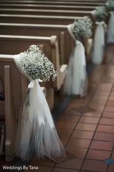 flowers are placed on the pews in this church wedding ceremony aisle line, with white tulle and baby's breath