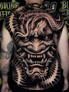 the back of a man's body with tattoos on it and an image of a demon