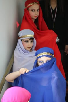 three women in red and blue veils standing next to each other with one woman covering her face