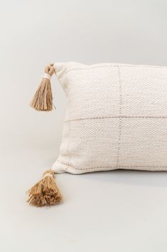 a white pillow with tassels on the side and a small brown tassel hanging from it