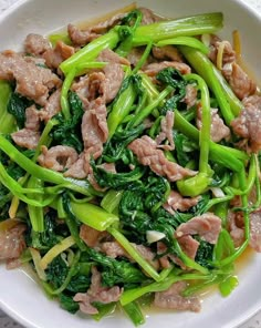 a white bowl filled with meat and green vegetables on top of a marble countertop