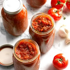 three jars filled with food sitting on top of a counter next to garlic and tomatoes