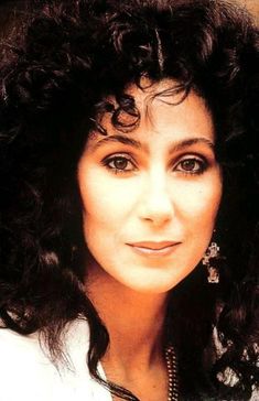 an old photo of a woman with curly hair and earrings on her head, smiling at the camera