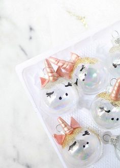 four glass ornaments with unicorn faces and bows on them sitting on a white tablecloth