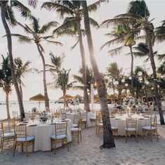 tables set up on the beach under palm trees for an outdoor wedding reception at sunset