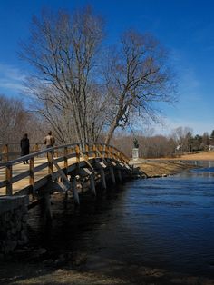 two people walking across a bridge over a river next to a park with trees in the background