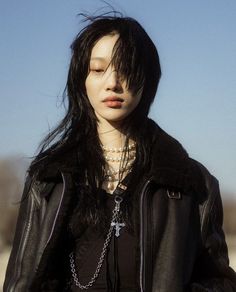 a woman with long black hair wearing a leather jacket and cross pendants on her necklace