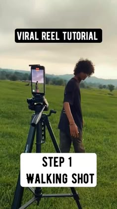 a man standing next to a camera on top of a tripod in a field