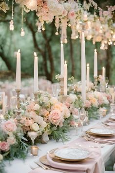 a long table topped with lots of pink flowers and white plates covered in candles next to each other