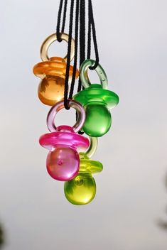 an assortment of colored glass beads hanging from a black cord with trees in the background