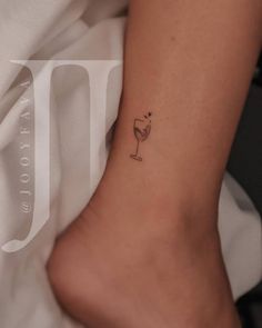 a woman's foot with a small wine glass tattoo on her left side ankle