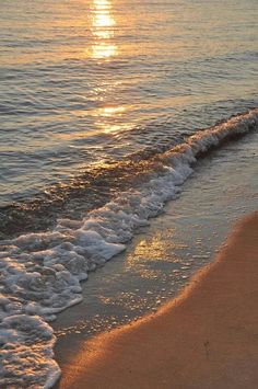 the sun is setting over the ocean with waves coming in to shore and an orange frisbee on the beach