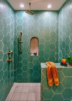 a green tiled bathroom with orange towels on the shelf and shower head in the corner