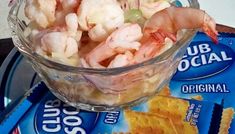 a glass bowl filled with shrimp and chips on top of a table next to a bag of chips