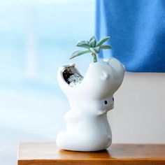 a small white elephant planter with a tiny green plant in it's mouth