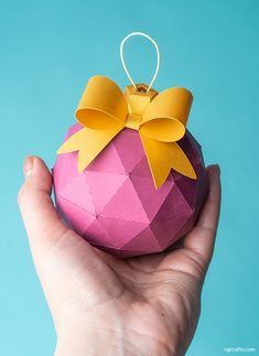 a hand holding a pink ornament with yellow bows on it's top