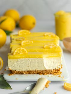 a slice of lemon cheesecake on a plate next to sliced lemons and a glass of orange juice