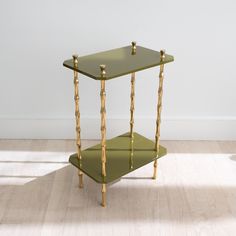 a small green table with gold trimmings on the top and bottom, against a white wall