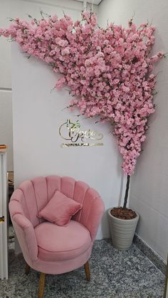 a pink chair sitting in front of a tree with pink flowers on it's branches