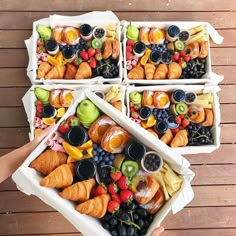 four white trays filled with fruit and pastries on top of a wooden table