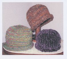 three knitted hats sitting on top of a wooden table next to a white wall