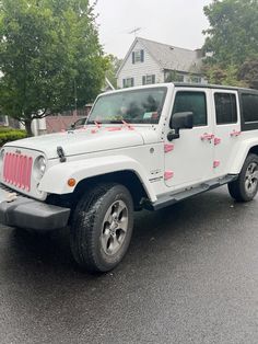 a white jeep parked in front of a house with pink bows on it's hood