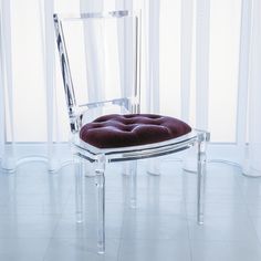 a clear chair sitting in front of a window next to a black cushion on the floor