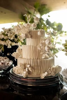 a three tiered cake with white flowers on the top and bottom, sitting on a table